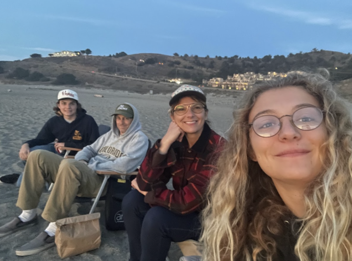 Margo with her family sitting in beach chairs on a Pacifica beach at dusk, with coastal hills behind them